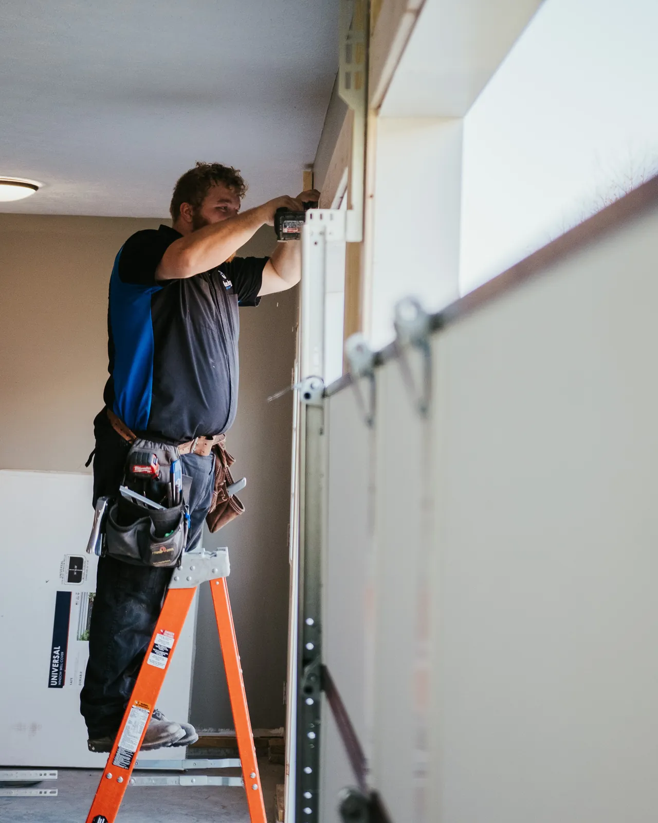 Blue Jay installer fitting hardware at the upper edge of a garage door