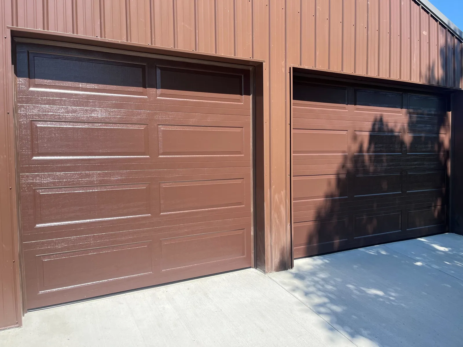 Brown raised-panel garage doors and trim in direct sunlight