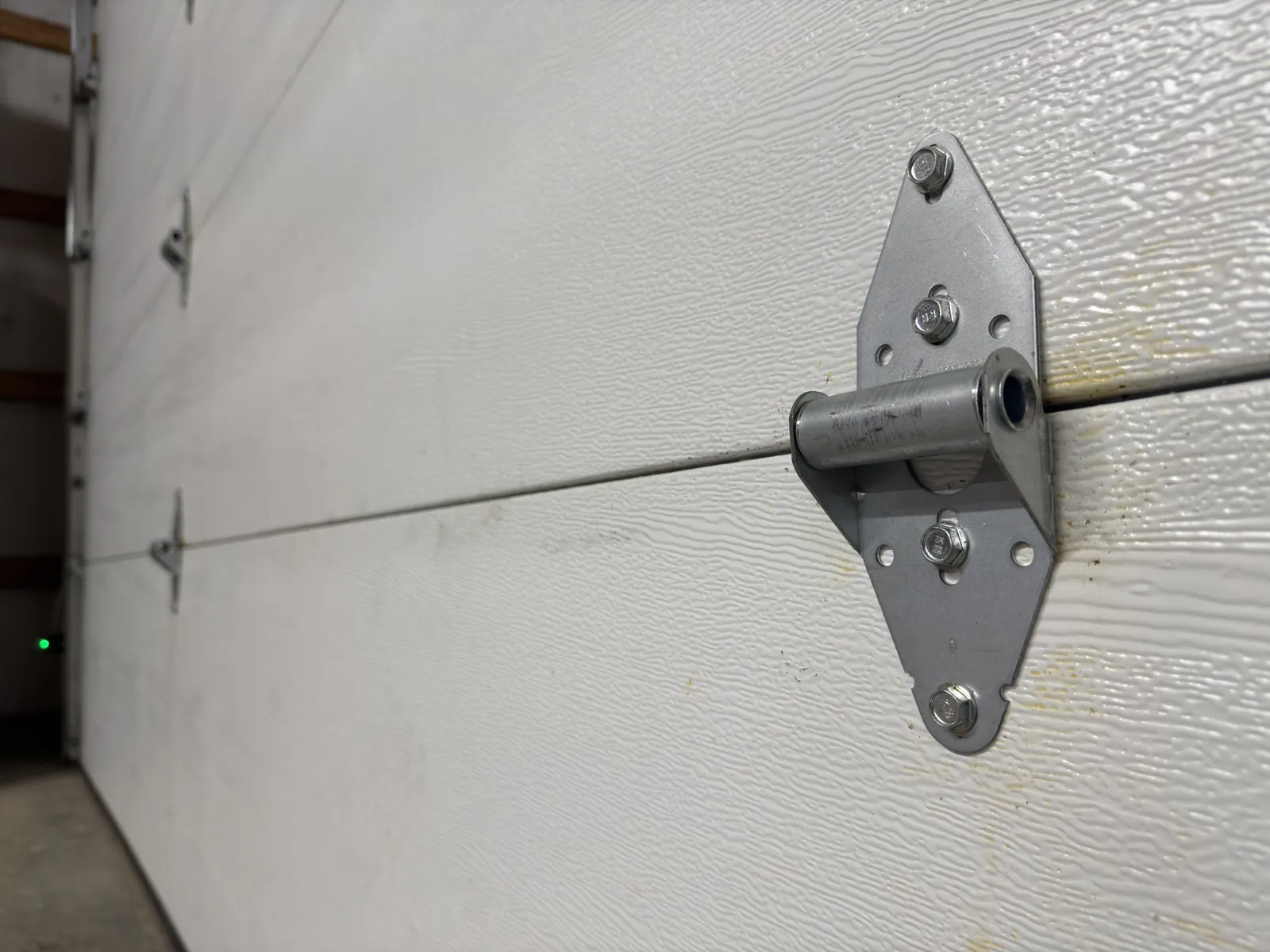 Steel hinge joining two white garage door sections