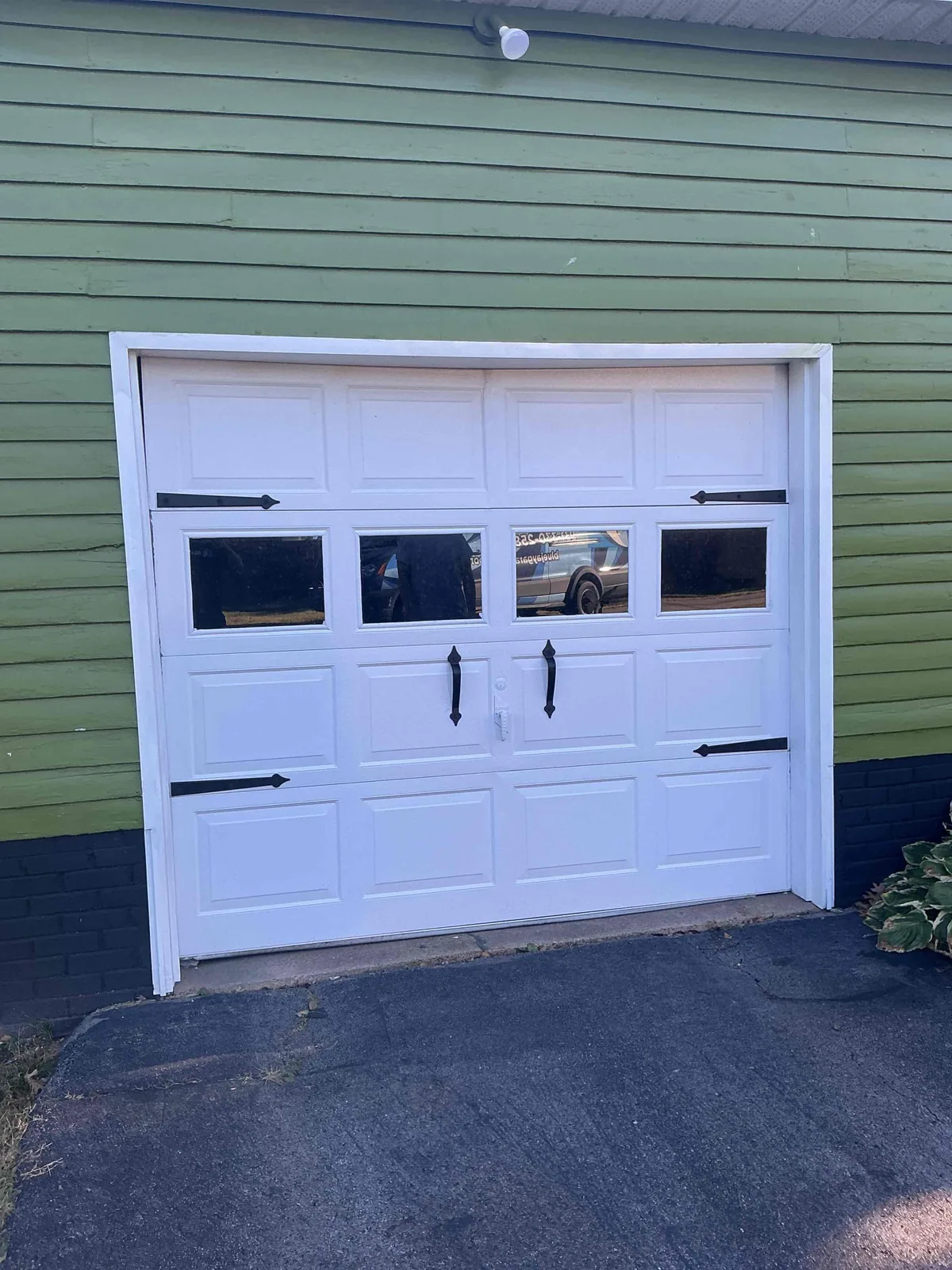 White garage door with four windows and black decorative hardware on a green-sided home