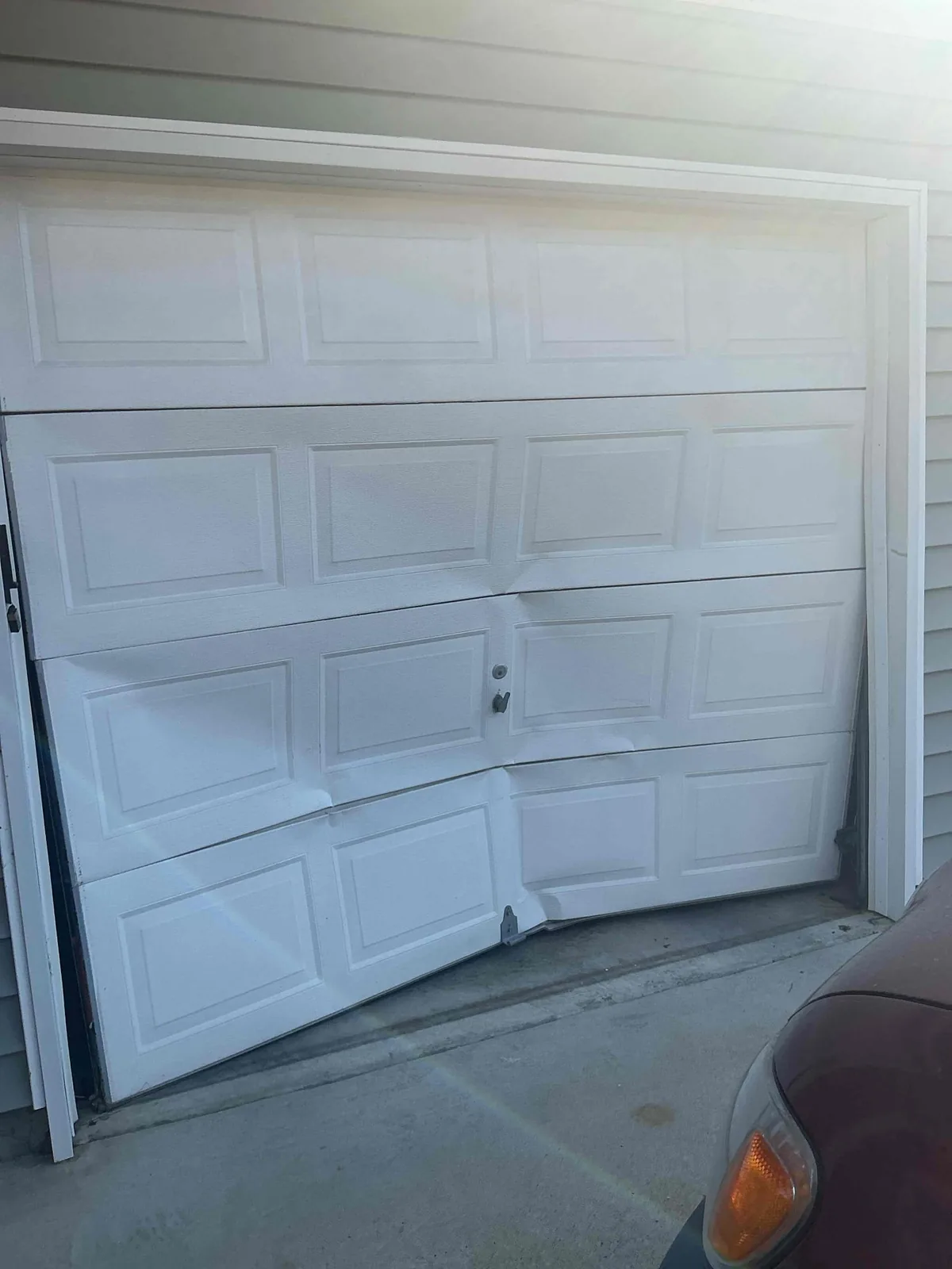 White sectional garage door with bent lower panels and an uneven bottom edge