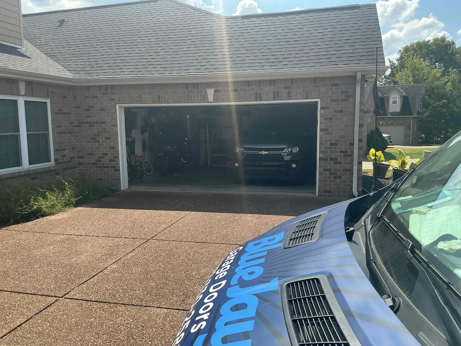 Blue Jay service van beside an open garage on a brick home