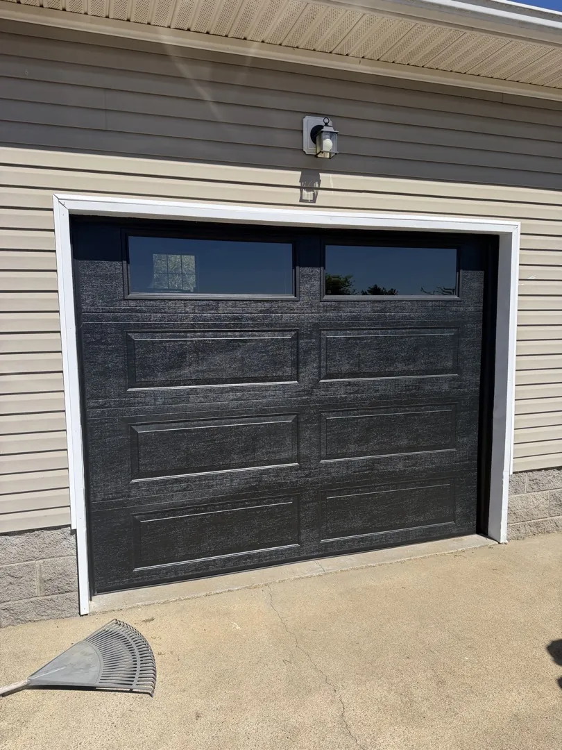 Dark wood-look garage door with top windows on the same sided home after replacement