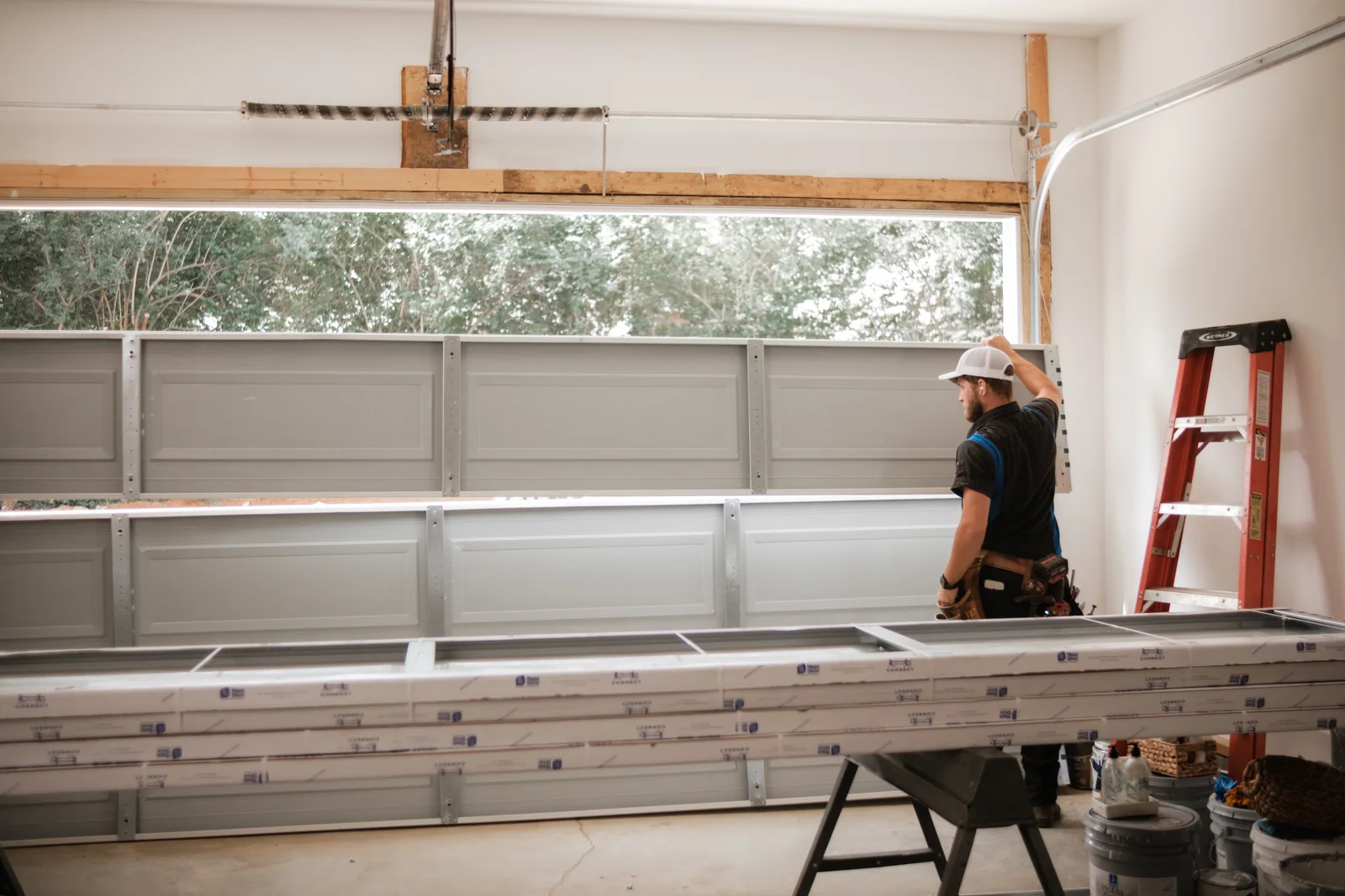Blue Jay installer fitting new garage door sections inside a garage, with a ladder nearby
