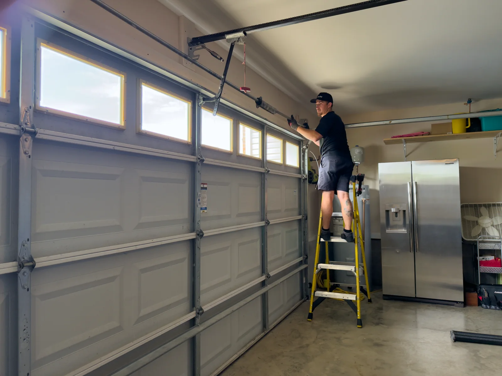 Blue Jay technician on a ladder working on the hardware above a closed garage door