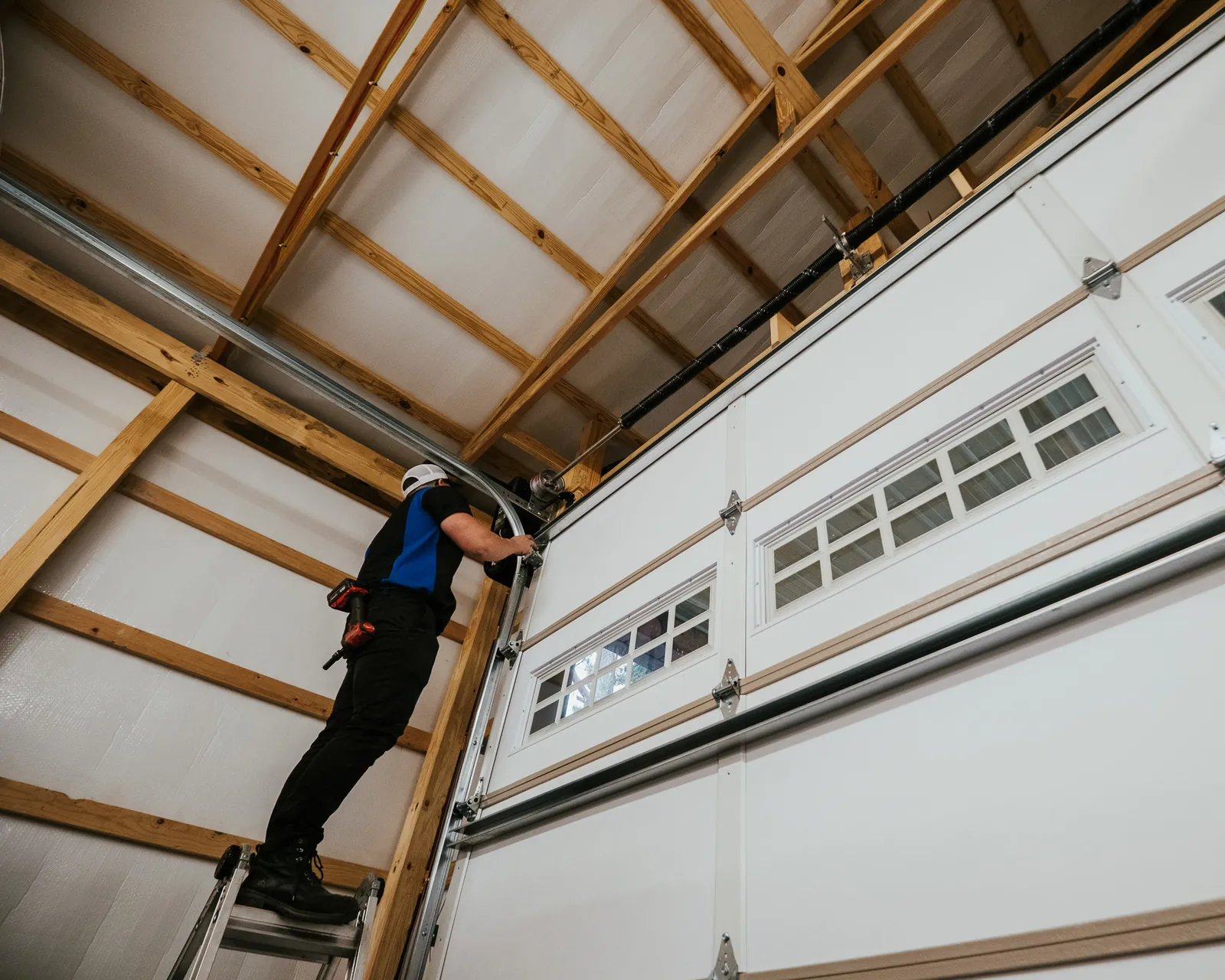Blue Jay installer working on the upper track of a white garage door
