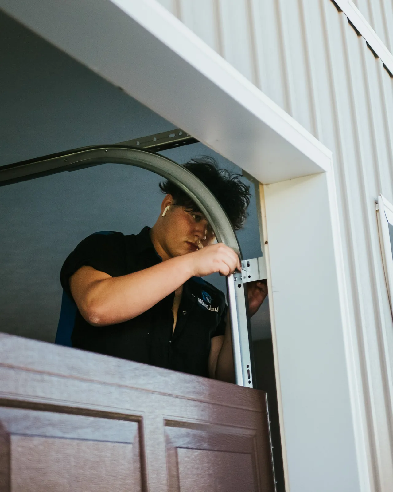 Blue Jay installer fitting a curved track beside a wood-look garage door