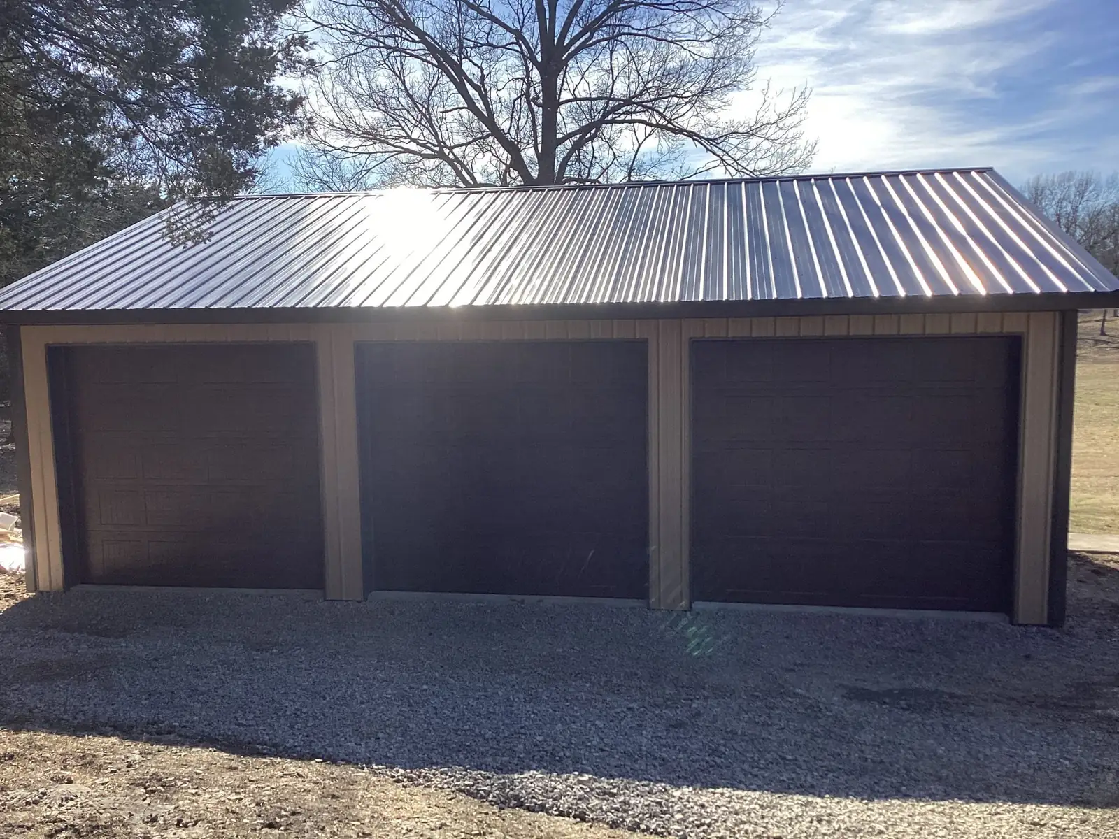 Three brown garage doors beneath a metal roof