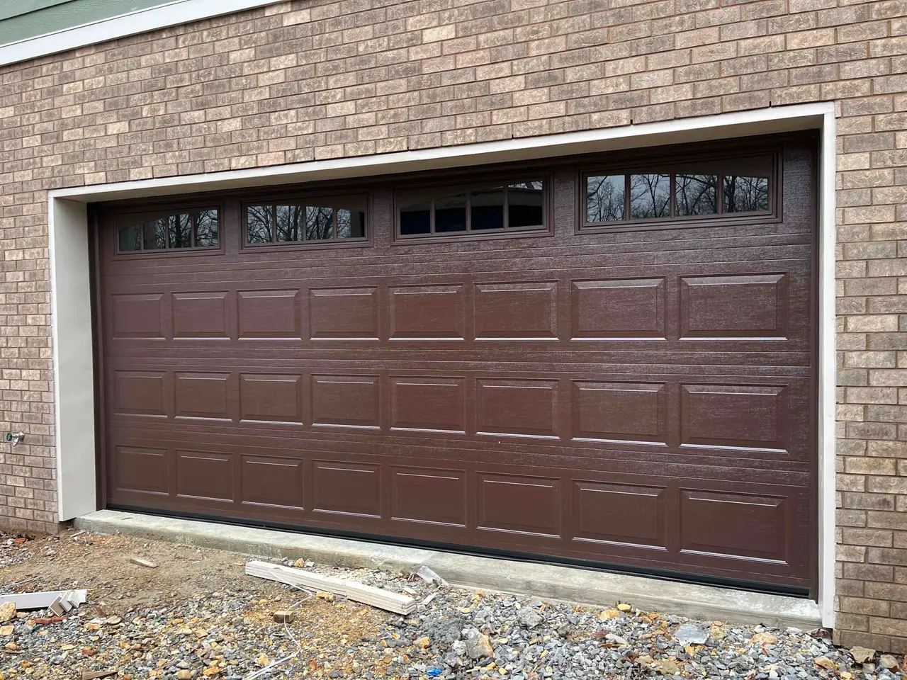 Brown carriage-style garage door with decorative hardware on a brick home