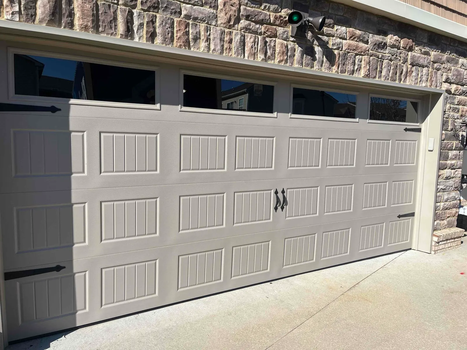 Tan carriage-style garage door beneath a stone wall